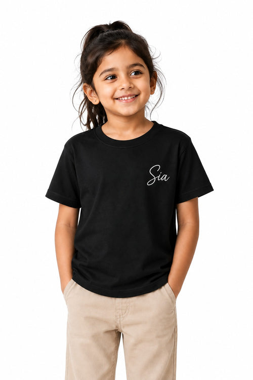 A young girl wearing a black Euphor Bliss crew neck cotton t-shirt with white cursive text, paired with beige pants.